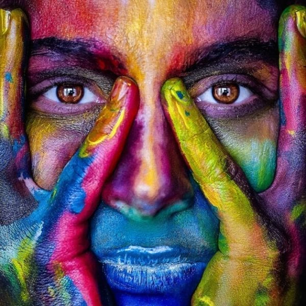 girl covered in colourful paint holding her face