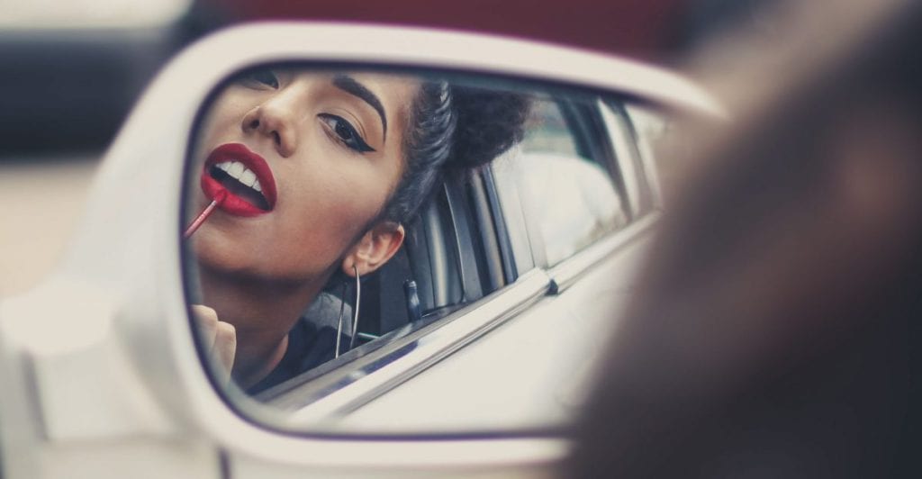 girl applying lipgloss in the car mirror