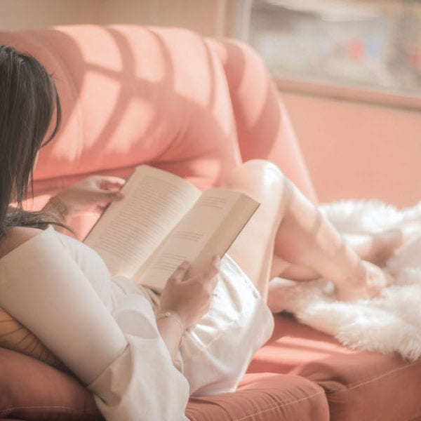 woman sitting in pink sofa reading a book