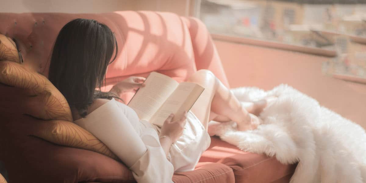 woman sitting in pink sofa reading a book