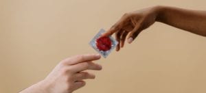 a hand giving another hand a condom