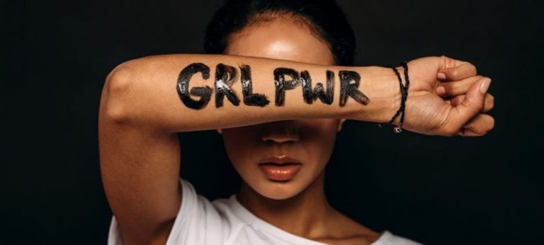 woman covering her face with her arm which has GRL PWR in black written on it